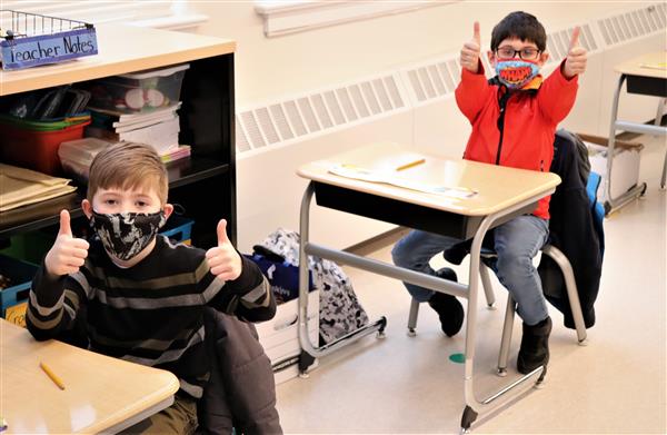 Two students at their desk wearing masks giving the camera two thumbs up.